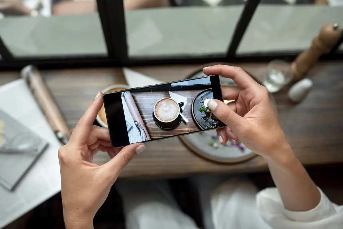 Personne prenant une photo d'une tasse de café et d'un plat sur une table avec un smartphone.