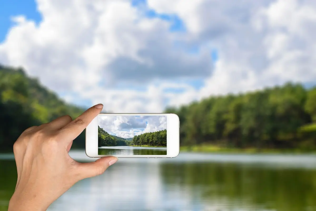 Personne prenant une photo d'un paysage de lac et de collines avec un smartphone.